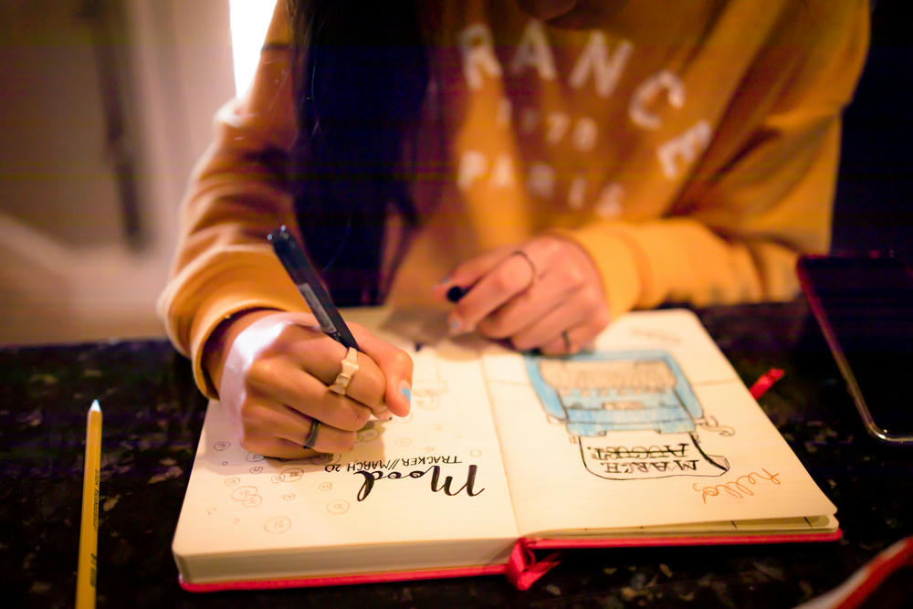 Closeup of young girl writing in bullet journal on mood tracker page.