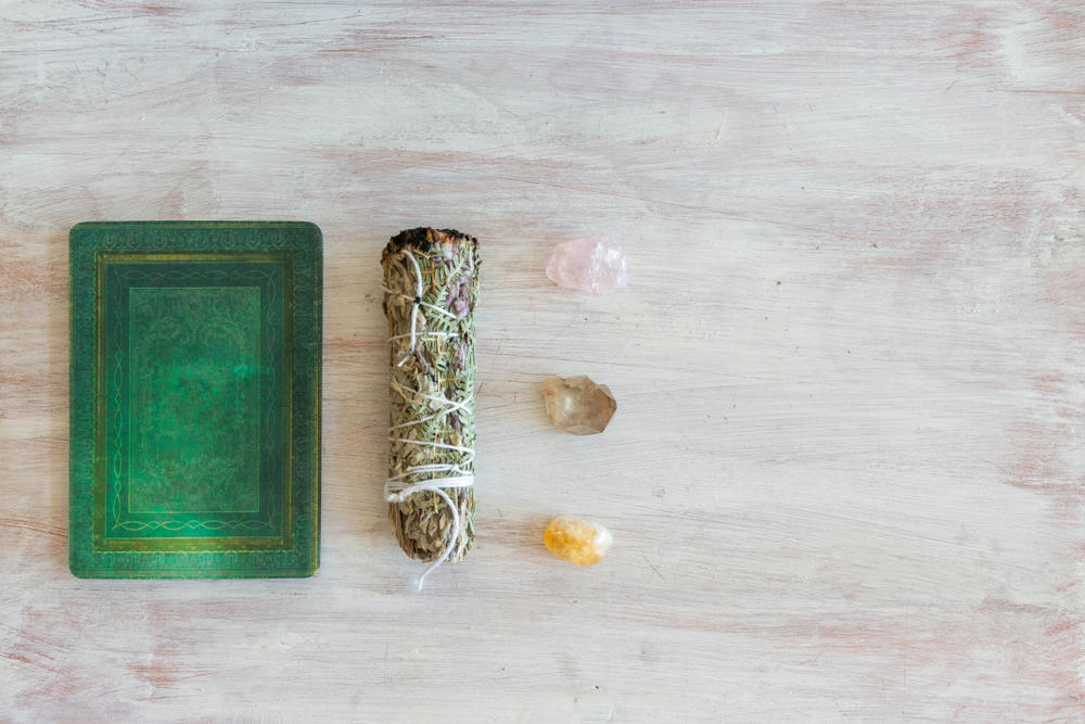 A deck of tarot cards with a sage stick and three crystals against a white-washed wood background.