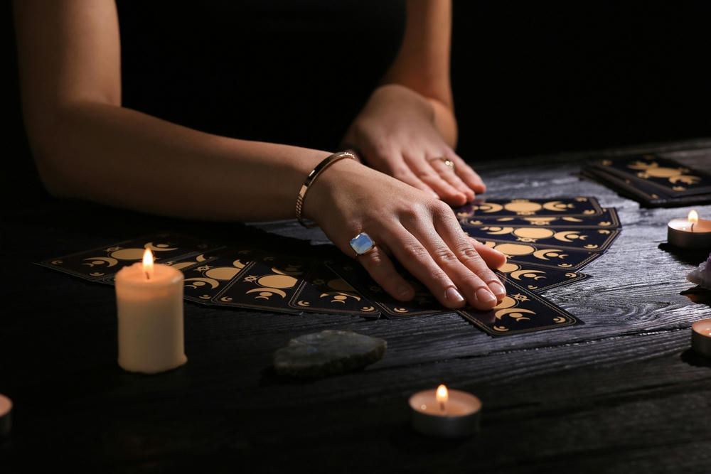 A soothsayer predicts the future with tarot cards at the table in darkness.