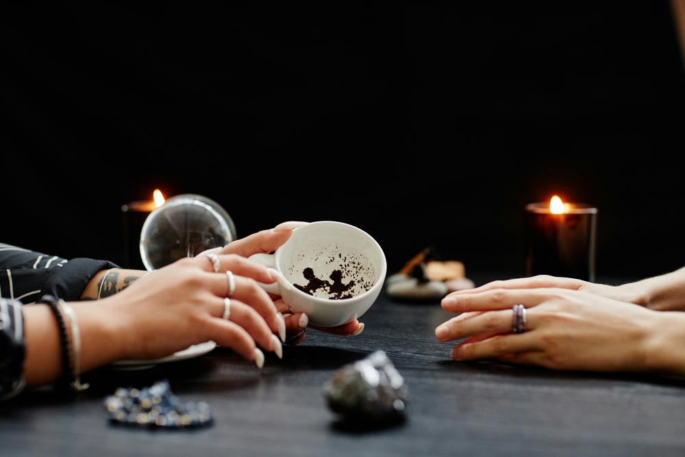 Side view close up of female fortune teller reading coffee grounds telling destiny in a seance with a young woman in dark.
