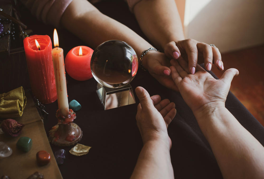 Palm reader at a seance fortune telling on a hand, candles and fortune-telling witch objects surround.